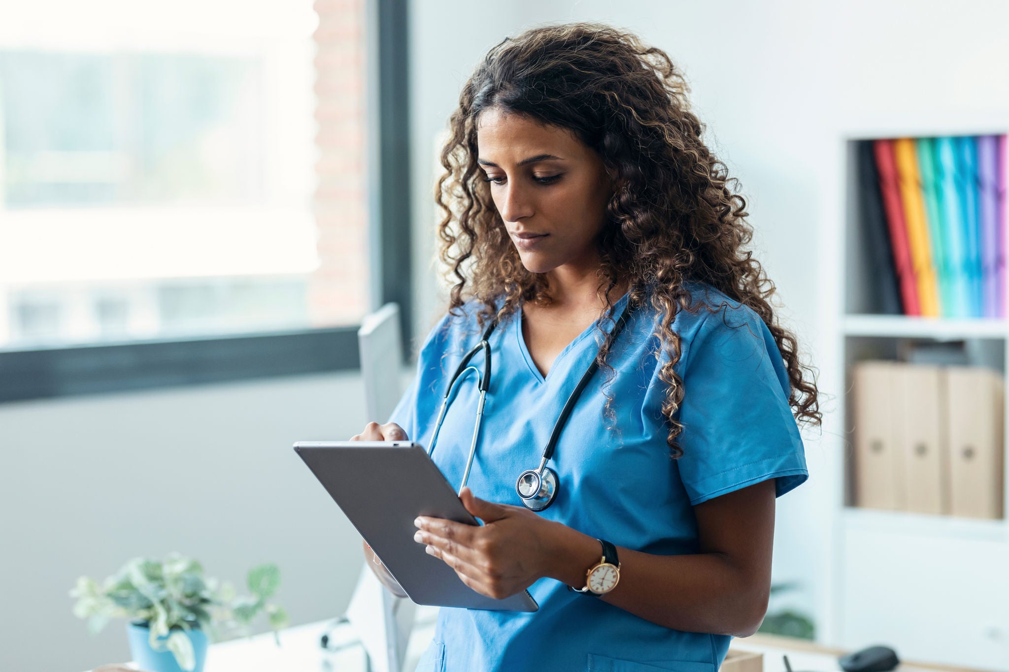 Shot of female nurse using her digital tablet while standing in the consultation.